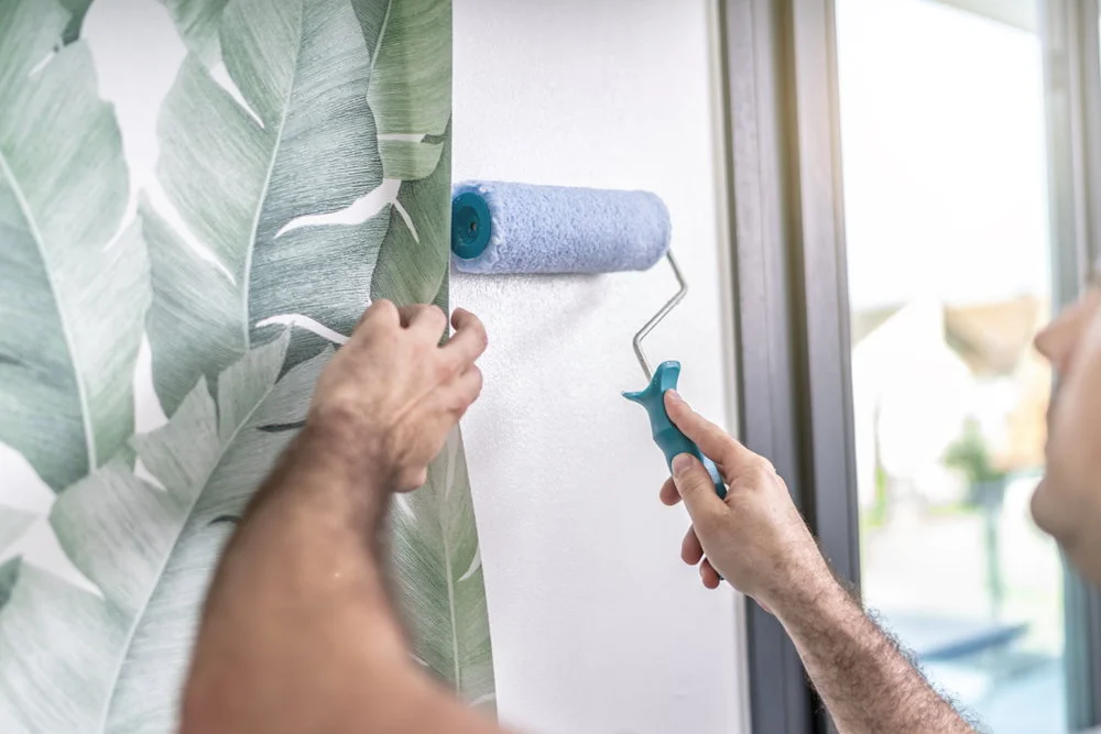 Person bringt mit einer Rolle Tapete an